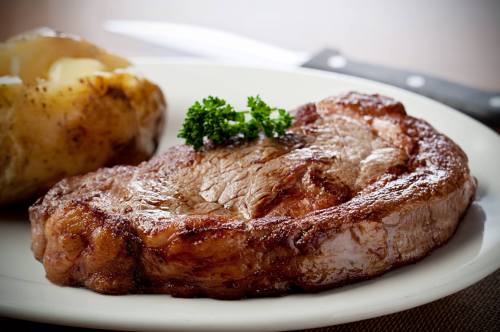 A juicy steak garnished with parsley, served alongside a baked potato on a white plate.