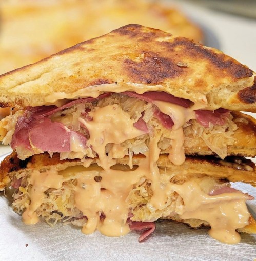 A stacked sandwich with layers of corned beef, sauerkraut, and melted cheese, drizzled with a creamy sauce.