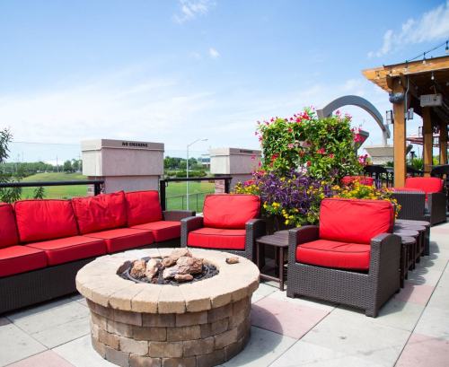 Outdoor seating area with red cushions, a stone fire pit, and vibrant flowers under a clear blue sky.
