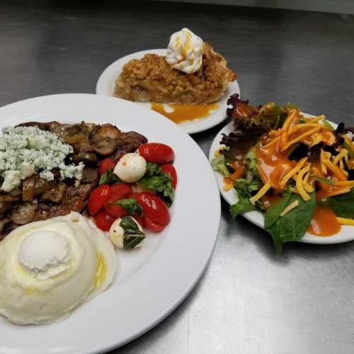 A plate of steak with mushrooms, mashed potatoes, cherry tomatoes, and a side salad, accompanied by a dessert.