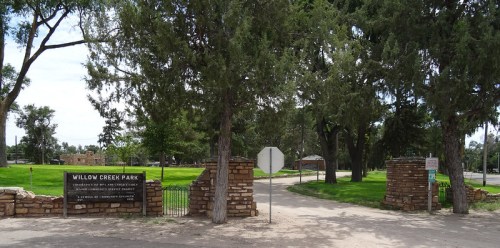 Entrance to Willow Creek Park, featuring stone pillars, trees, and a sign welcoming visitors.