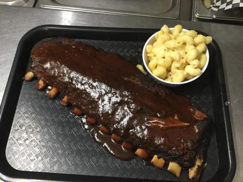 A large serving of barbecue ribs with a rich sauce, accompanied by a bowl of macaroni and cheese on a black tray.