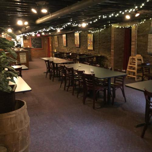A dimly lit restaurant interior with tables, chairs, and string lights along the ceiling, featuring stone walls and artwork.