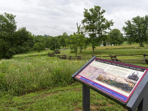 A historical marker in a grassy field, with trees and a distant house, detailing the Assault from the Bottom House.