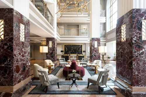 Elegant hotel lobby featuring marble columns, stylish seating, and modern decor with a grand chandelier.