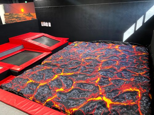 A trampoline area featuring a large lava-themed landing pad and red safety edges.