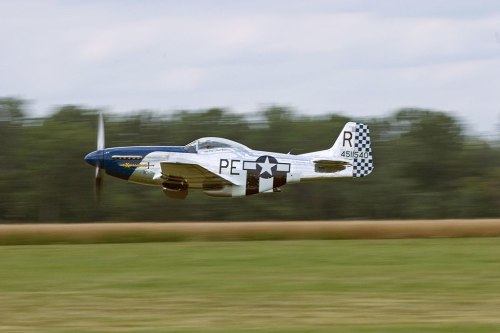 A vintage fighter plane flying low over a grassy field, showcasing a blue and white checkered tail and star insignia.