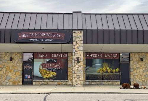 Storefront of Al's Delicious Popcorn, featuring a stone facade and large windows displaying popcorn and the establishment year, 1983.