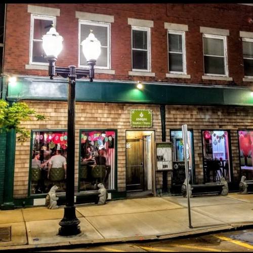 A cozy restaurant exterior at night, featuring decorative lights and a welcoming entrance with people inside.