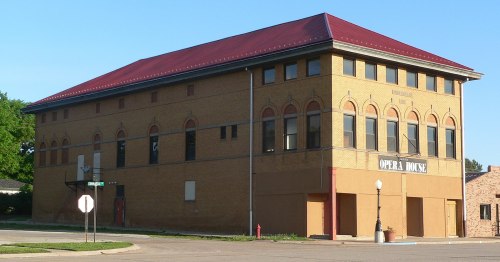 Historic brick building with a red roof, labeled "Opera House," located at a street corner.