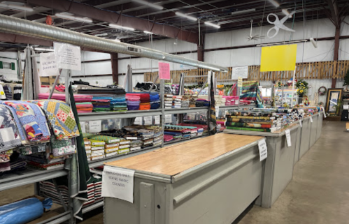 A spacious fabric store interior with shelves of colorful fabrics and a wooden counter in the foreground.