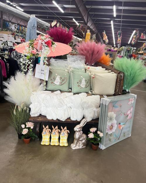 A display featuring decorative pillows, faux flowers, bunnies, and a floral painting in a retail space.