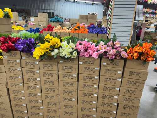 Colorful artificial flowers arranged in boxes, filling a warehouse space with vibrant hues.