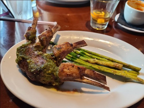 A plate featuring grilled lamb chops with a green herb sauce and asparagus on the side.