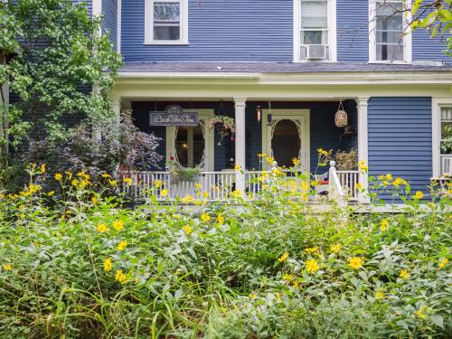 A charming blue house with white trim, surrounded by vibrant yellow flowers and greenery.