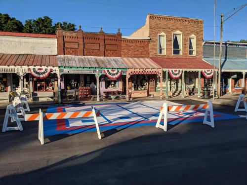 A colorful street mural in a historic town, with festive decorations and construction barriers in place.