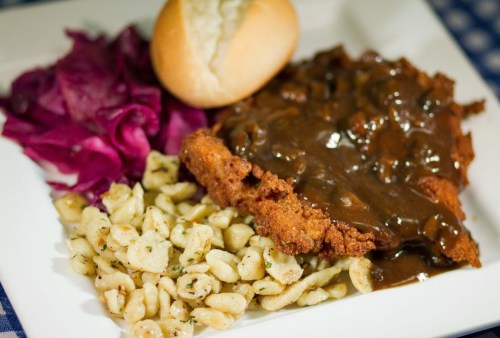 A plate featuring fried chicken with gravy, egg noodles, red cabbage, and a dinner roll.