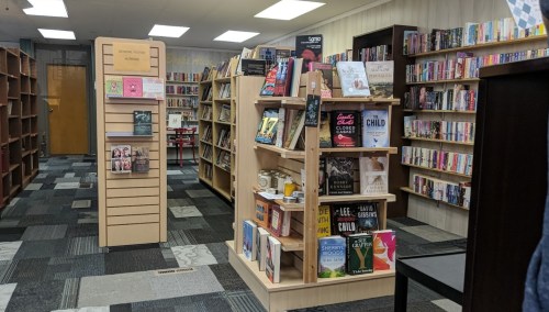 A cozy bookstore interior with wooden shelves filled with various books and a reading area in the background.