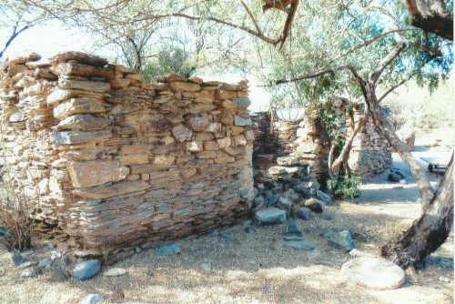 Ruins of stone structures surrounded by trees and rocky terrain, showcasing ancient architecture in a natural setting.
