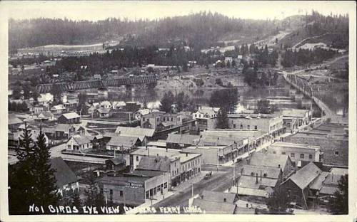 Black and white bird's-eye view of a small town with houses, a river, and a bridge in the background.