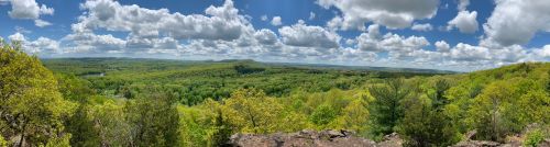 A panoramic view of lush green hills under a bright blue sky with fluffy white clouds.
