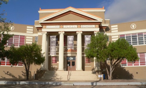 Front view of Bujan Plaza School, featuring large columns, banners, and trees in a sunny setting.