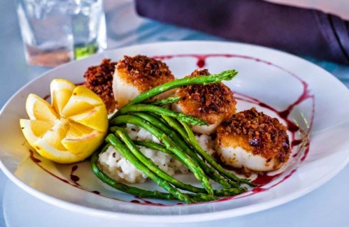 Plate of seared scallops with asparagus, lemon, and a drizzle of sauce, served over creamy risotto.