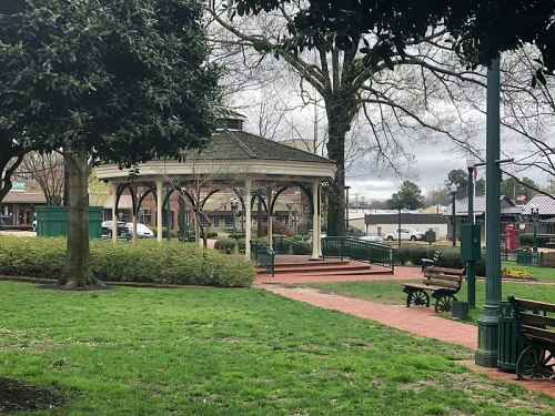 A park scene featuring a gazebo, benches, and green grass under cloudy skies.