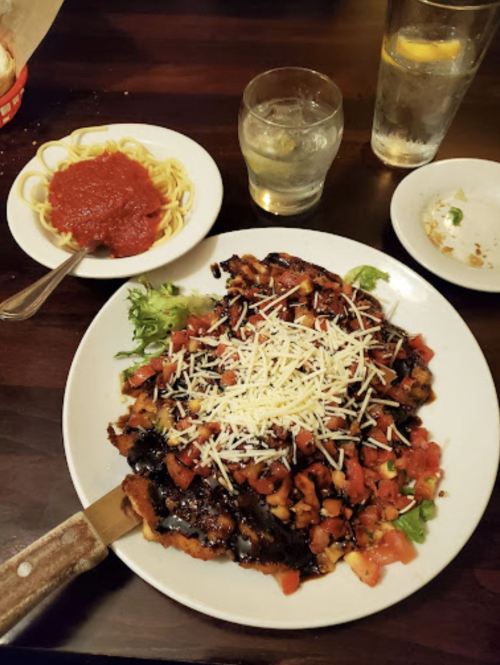 A plate of grilled chicken topped with diced tomatoes and cheese, served with spaghetti and marinara sauce on the side.
