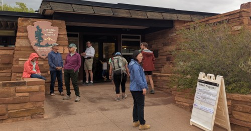 Visitors gather outside the stone Capitol Reef National Park Visitor Center under a cloudy sky in Utah.
