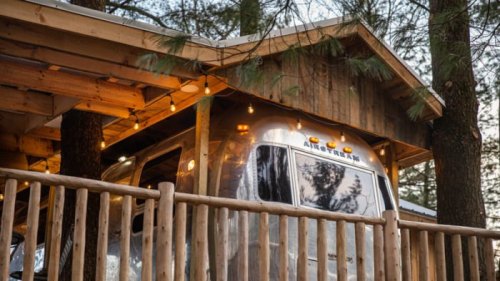 A cozy cabin with an Airstream trailer nestled among trees, adorned with string lights.