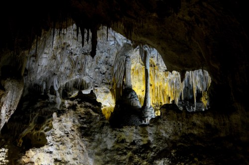 Stalactites and stalagmites illuminated in a dark cave, showcasing unique rock formations and textures.