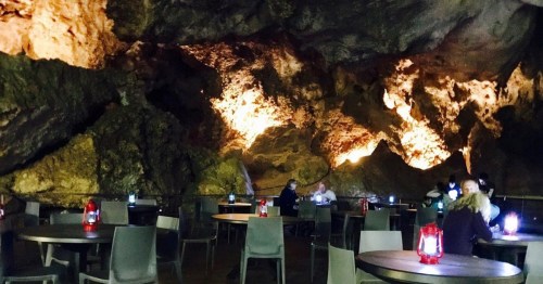 A dimly lit cave restaurant with stone walls, tables, and lanterns, creating a cozy atmosphere for diners.