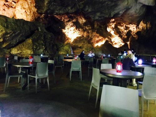 A dimly lit cave restaurant with tables and lanterns, featuring rocky walls and a cozy atmosphere.