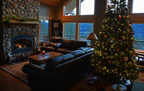 Cozy living room with a stone fireplace, decorated Christmas tree, and large windows showcasing a mountain view.