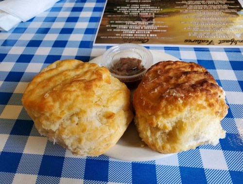 Two golden-brown biscuits on a plate, served with a small container of spread, on a blue and white checkered tablecloth.