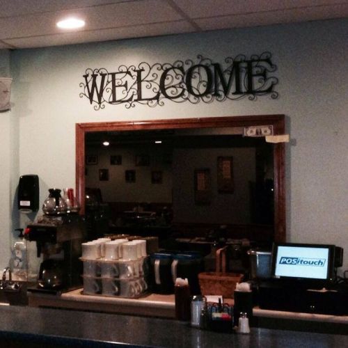 A cozy café counter with a "WELCOME" sign, coffee equipment, and a POS system in a warm, inviting atmosphere.