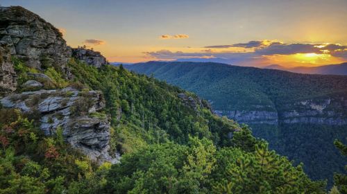 A scenic view of mountains and valleys at sunset, with rocky cliffs and lush greenery in the foreground.