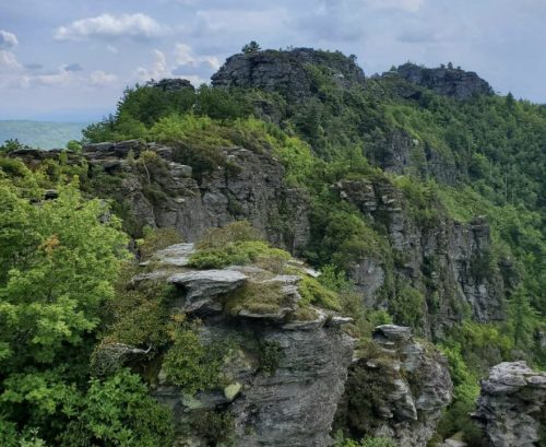 Lush green cliffs rise under a cloudy sky, showcasing rugged rock formations and dense foliage.