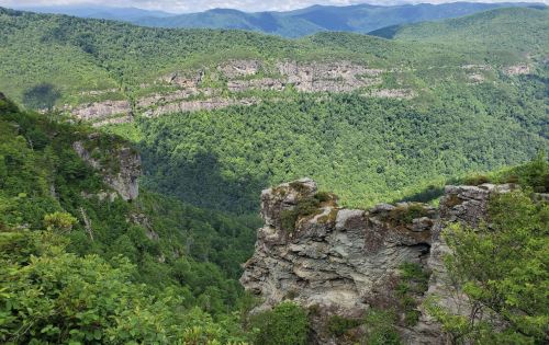 A panoramic view of lush green mountains and cliffs under a clear blue sky.