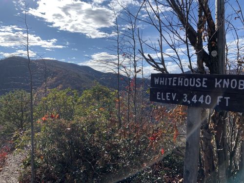 Sign for Whitehouse Knob at 3,440 ft elevation, with a scenic view of mountains and autumn foliage in the background.