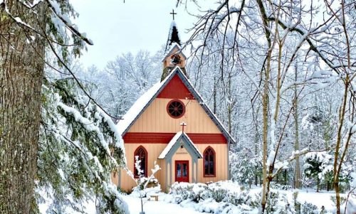 A quaint church surrounded by snow-covered trees and a winter landscape, creating a serene, picturesque scene.