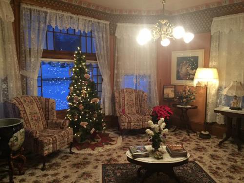 Cozy living room with a decorated Christmas tree, floral armchairs, and a warm glow from lamps, set against a snowy backdrop.