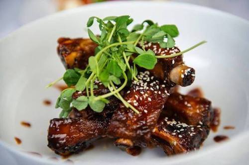 A plate of glazed ribs garnished with fresh greens and sesame seeds, served in a white bowl.