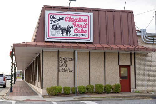 Exterior of Claxton Fruit Cake bakery, featuring a sign that reads "Old Fashion Claxton Fruit Cake World Famous."