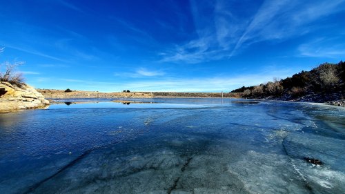 A serene landscape featuring a frozen lake under a clear blue sky, surrounded by rocky terrain and sparse vegetation.