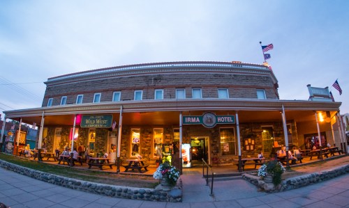 Historic Irma Hotel with outdoor seating, flags flying, and a lively atmosphere at dusk.
