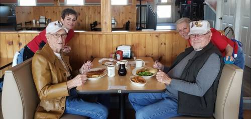 Four people enjoying a meal together at a restaurant, smiling and seated at a table with food and drinks.