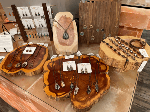Display of handcrafted jewelry on wooden stands, featuring necklaces and earrings in various styles and materials.