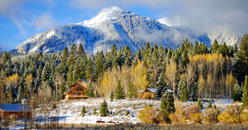 A snowy mountain landscape with evergreen trees, colorful autumn foliage, and cozy cabins in the foreground.